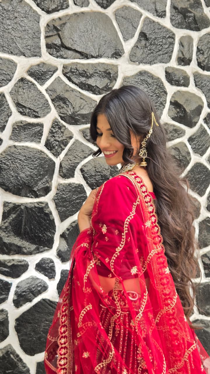 Bhakti in a red embroidered lehenga with gold jewellery, smiling down against a black and white stone wall