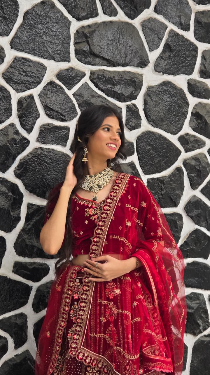 Bhakti in a deep red velvet lehenga and statement necklace, smiling to the side