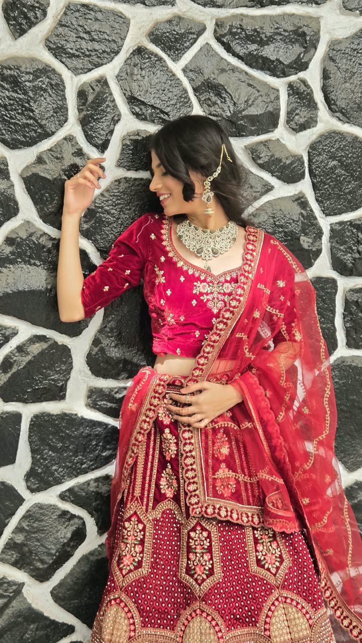 Bhakti in a red velvet lehenga leaning against a black stone wall, laughing