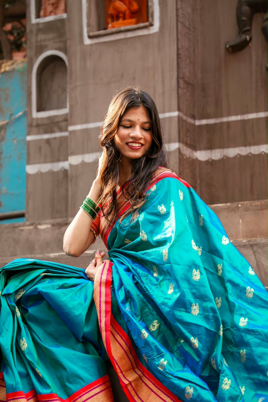 Bhakti looking down and smiling in a teal silk saree with gold peacock motifs