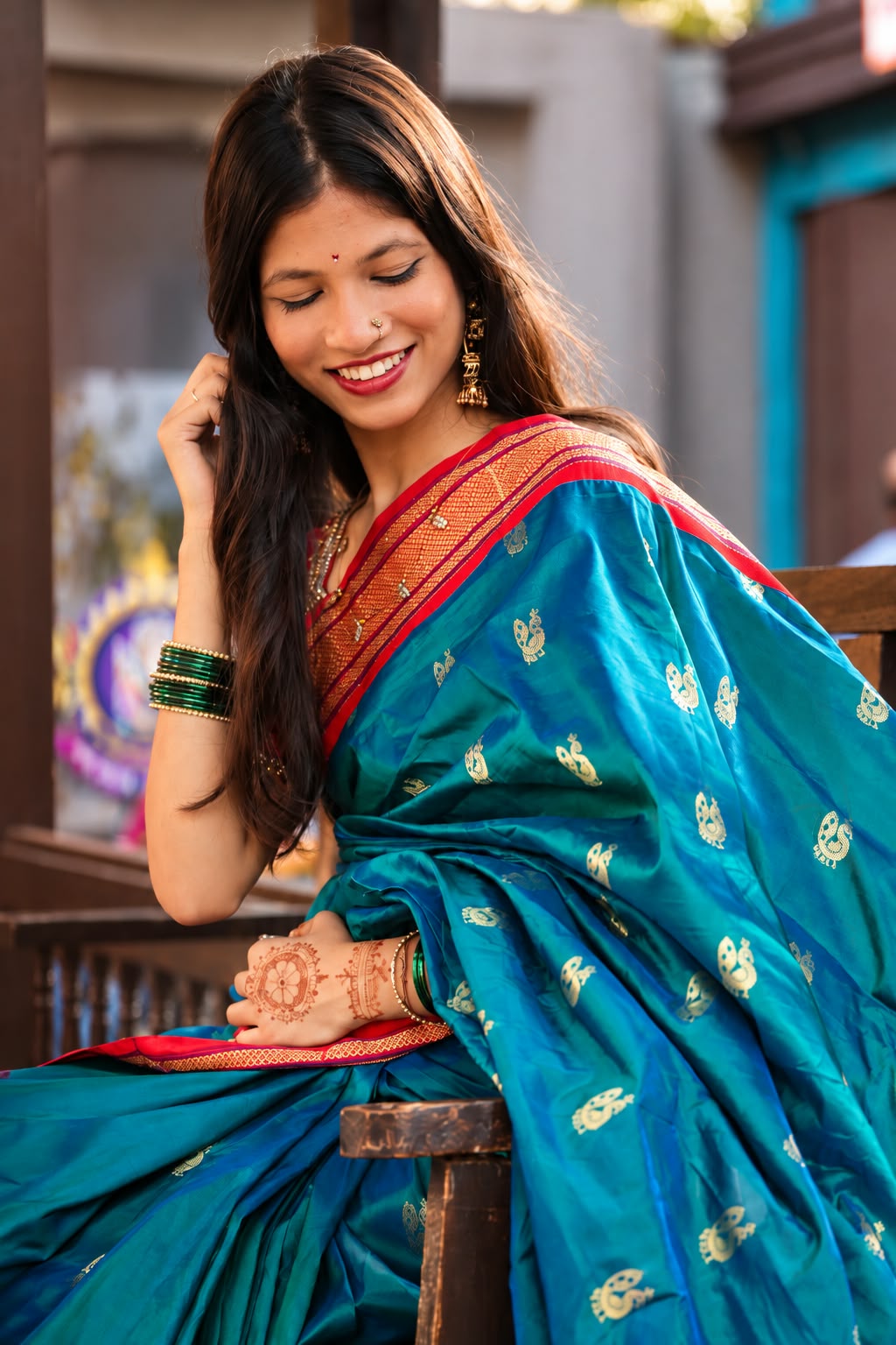Bhakti seated in a teal silk saree, smiling down with her hand in her hair, in warm golden light