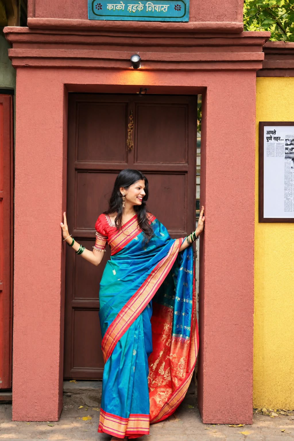 Bhakti standing in a doorway in a blue and red silk saree, hands on the frame