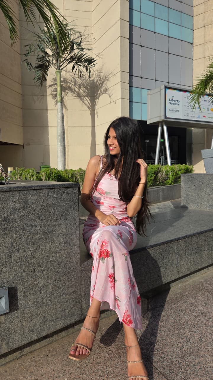 Bhakti in a pink floral dress, sitting on a stone ledge and looking away