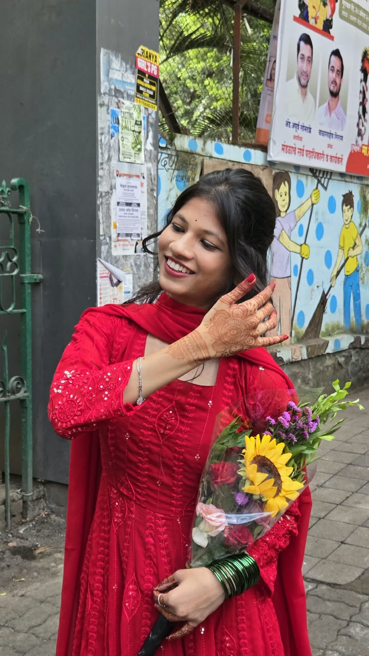 Bhakti in a red embroidered suit with henna-decorated hands, holding a bouquet of sunflowers and roses