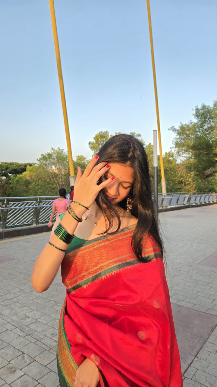 Bhakti in a red saree with green bangles, her hand raised to her face on a pedestrian bridge