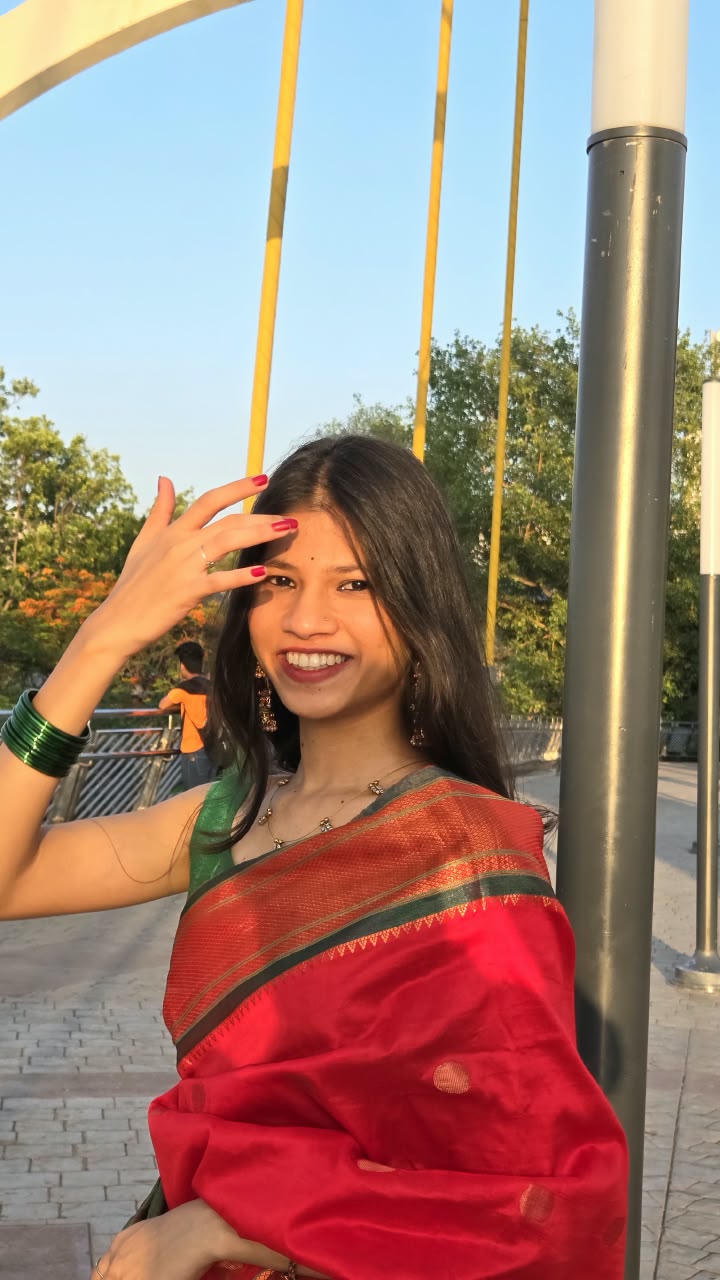 Bhakti smiling at the camera in a red saree on a sunlit bridge