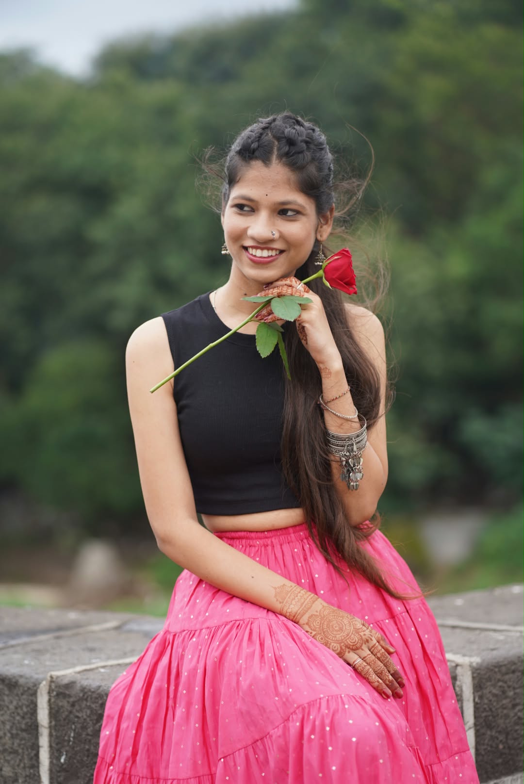 Bhakti in a black top and pink skirt, holding a red rose and smiling
