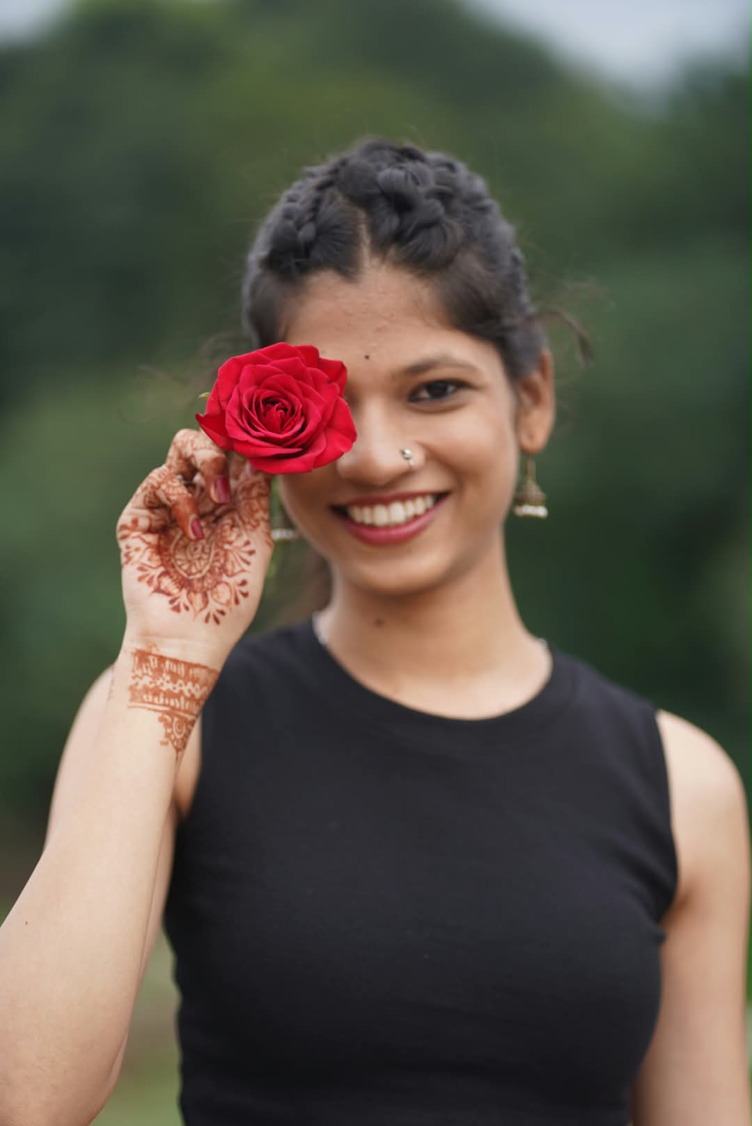 Bhakti holding a red rose in front of one eye, smiling