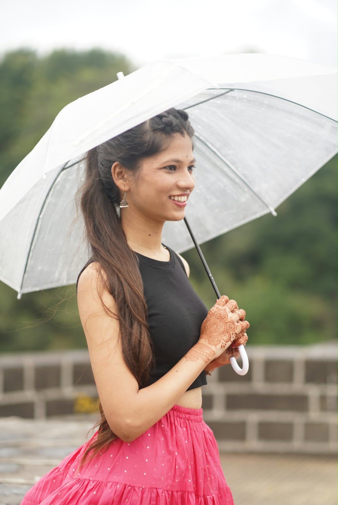 Bhakti holding a clear umbrella, smiling in soft rainy light