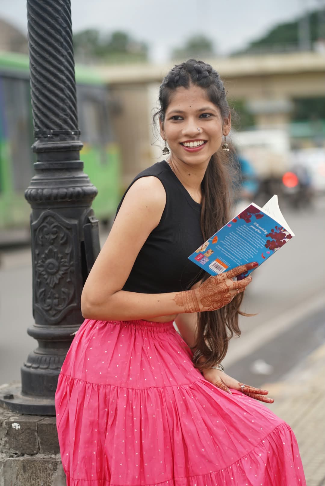 Bhakti holding an open book beside a street lamp, smiling over her shoulder